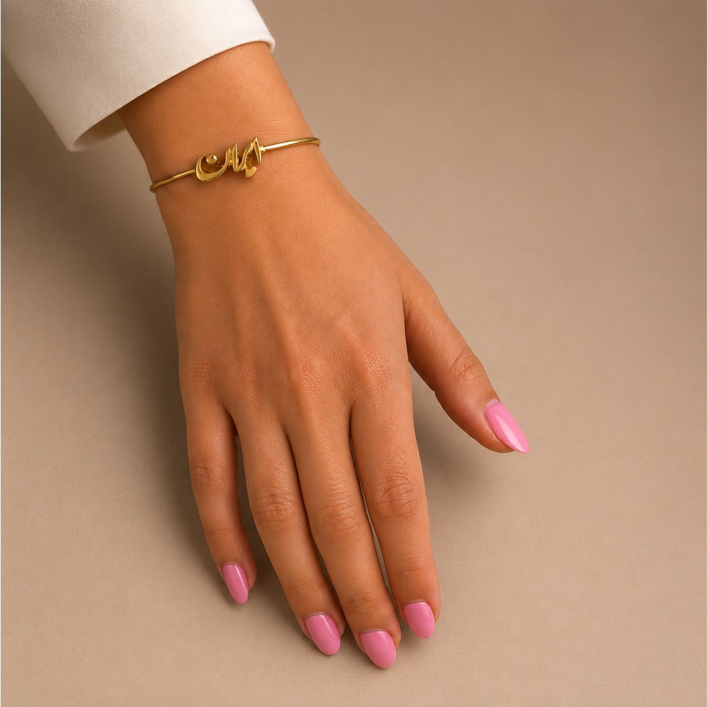 Adjustable gold-tone Iran script bangle bracelet worn on a woman's wrist with a minimalist neutral background.
