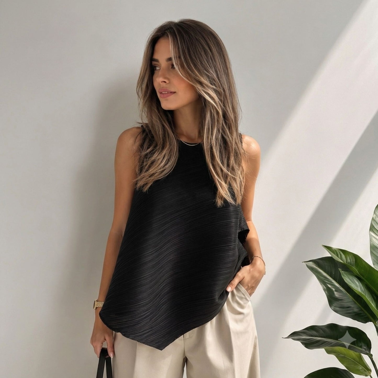 Model wearing a black pleated asymmetric sleeveless top with a flowing silhouette, crew neckline, and modern one-size fit.