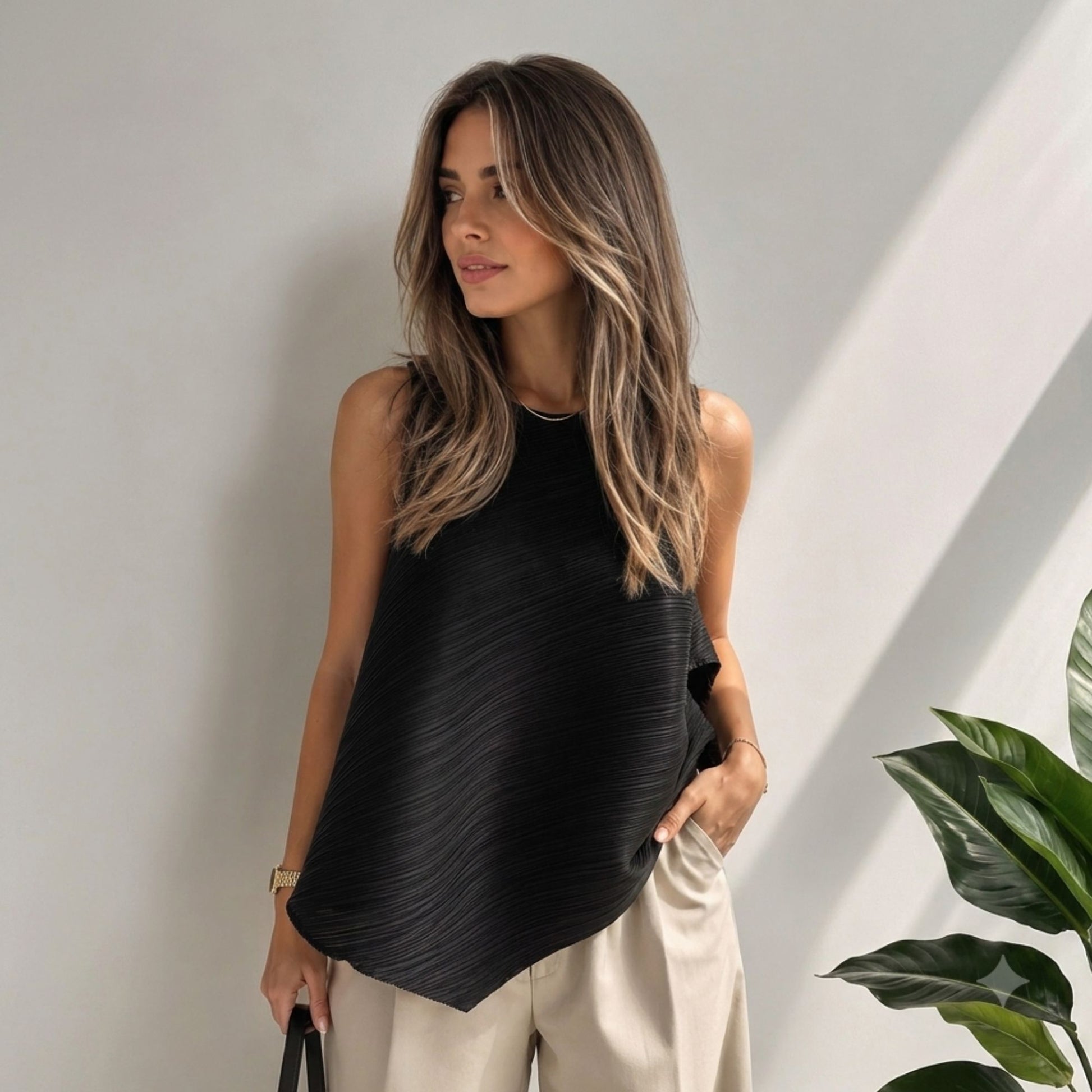 Model wearing a black pleated asymmetric sleeveless top with a flowing silhouette, crew neckline, and modern one-size fit.