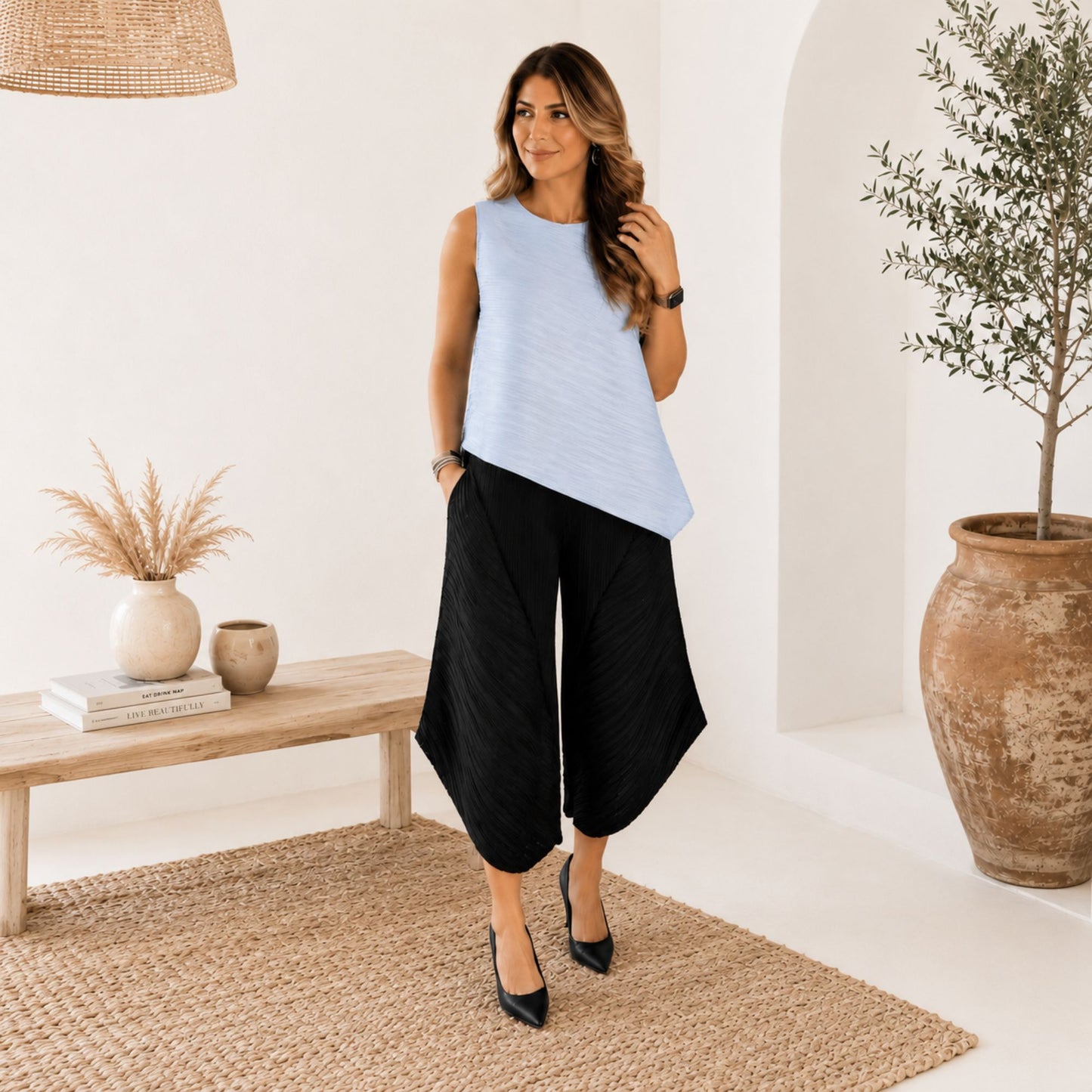 Model wearing a blue pleated asymmetric sleeveless top with a flowing silhouette, crew neckline, and modern one-size fit