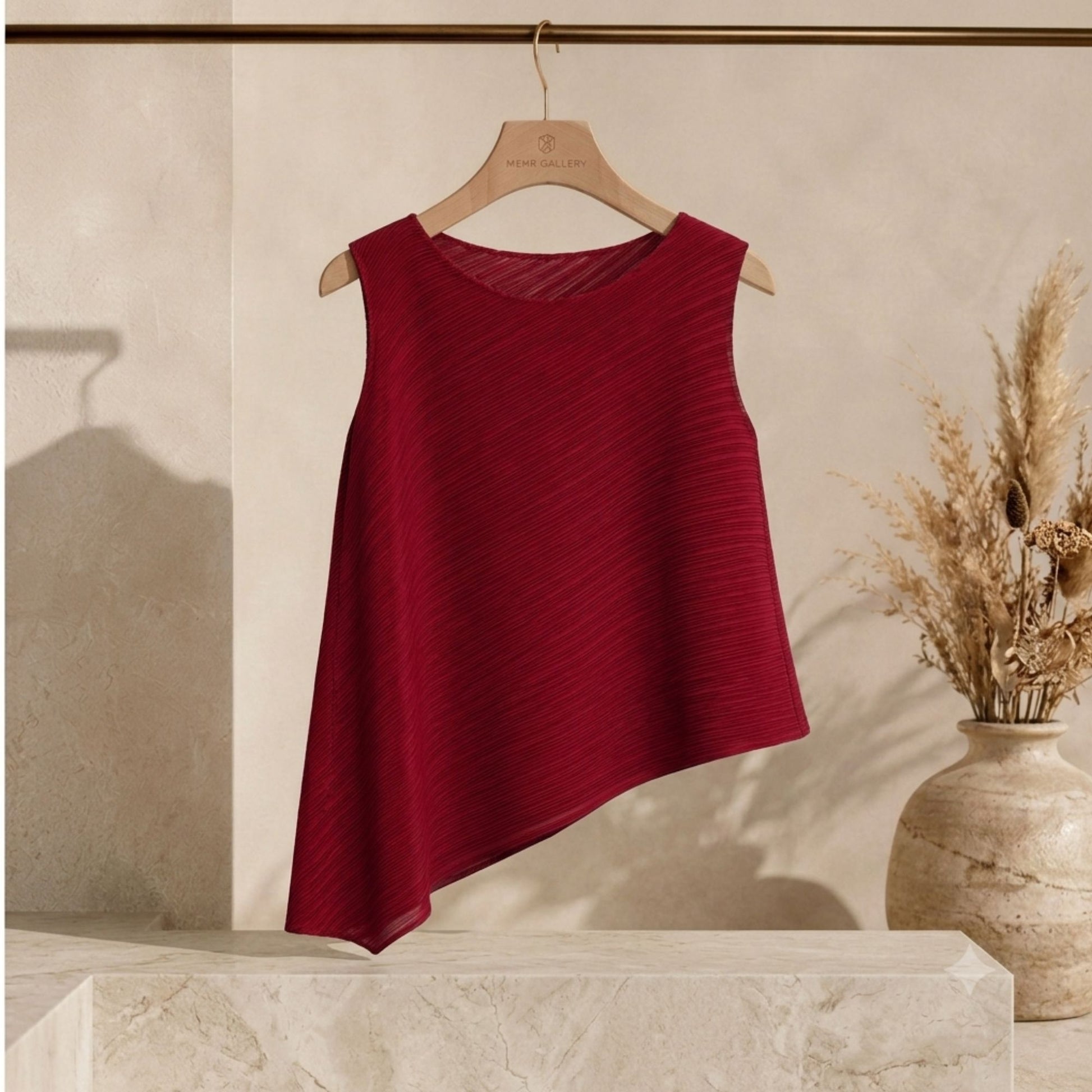 Burgundy pleated sleeveless top displayed on a hanger featuring an asymmetric hemline, crew neck, and wrinkle-resistant fabric.