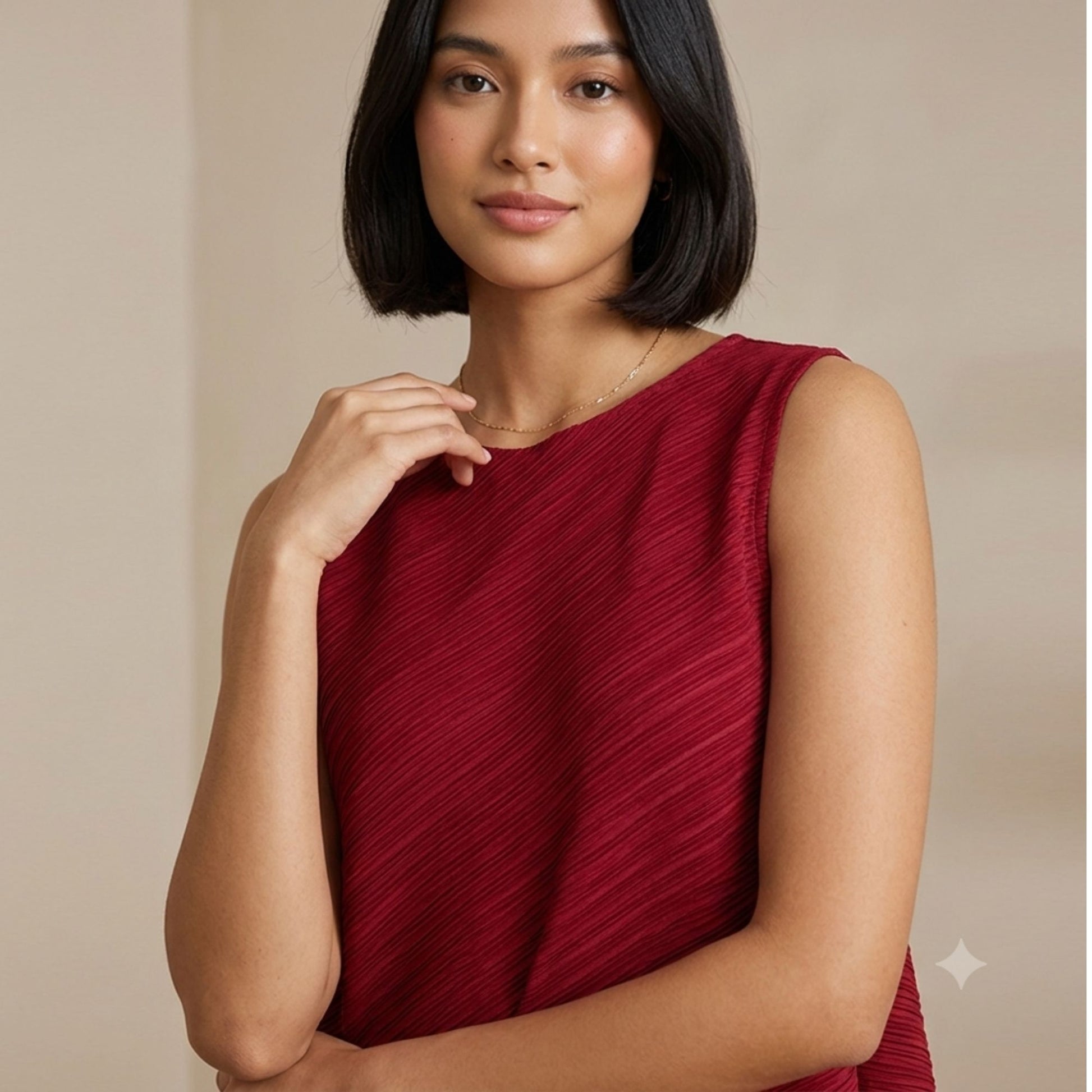Woman styling a burgundy pleated sleeveless top with an asymmetric hem, lightweight fabric, and contemporary design.