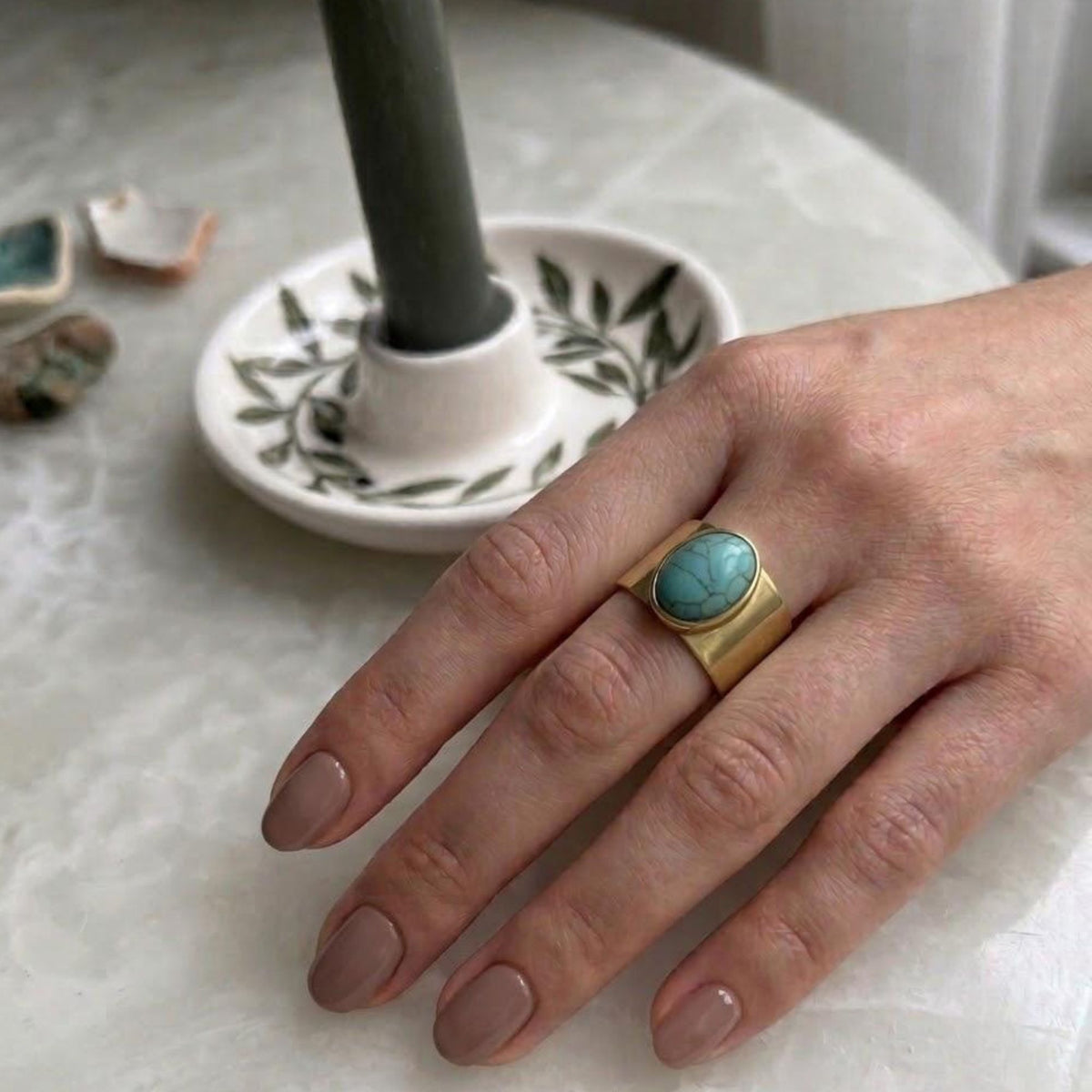 Hand wearing a wide gold-tone ring with an oval turquoise-look accent.