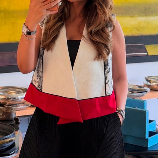 Woman wearing a geometric print sleeveless wrap vest with a white pleated front, red hem detail, and black dress for a modern elegant look.