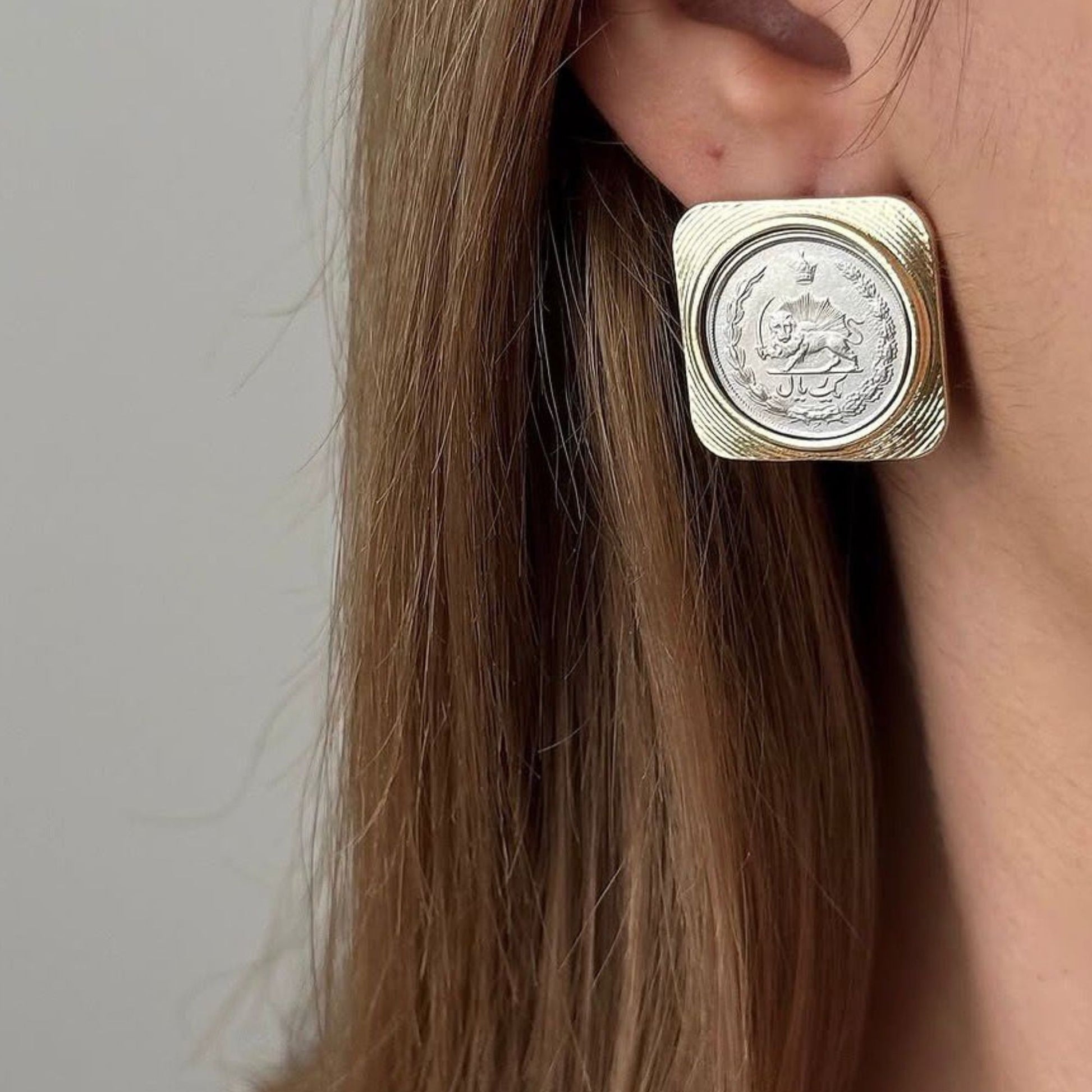 Close-up of square gold frame earrings with Pahlavi era coin