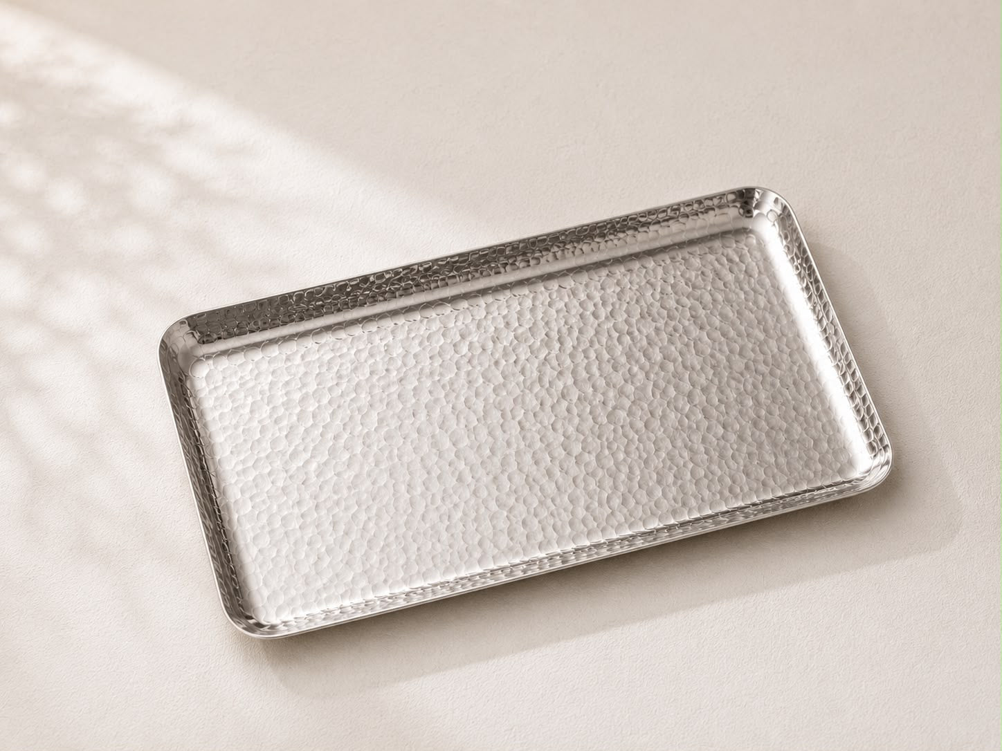 A rectangular metal tray with a hammered or textured finish, shown on a light beige surface with soft shadows.
