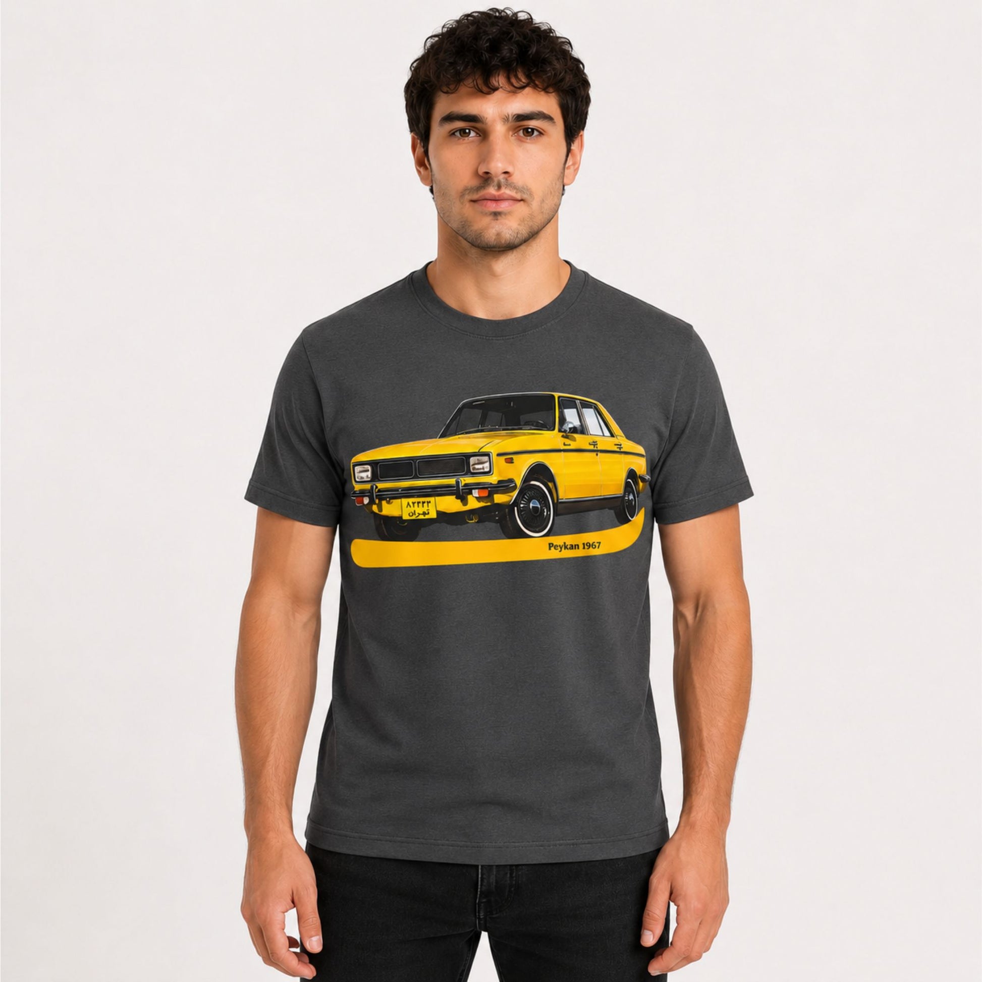 Male model wearing a dark gray Peykan 1967 vintage car graphic t-shirt with a retro yellow classic car illustration.