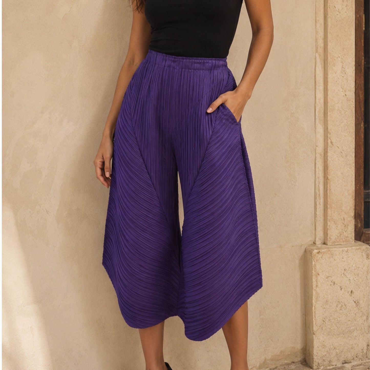Person wearing purple pleated pants against a beige wall.