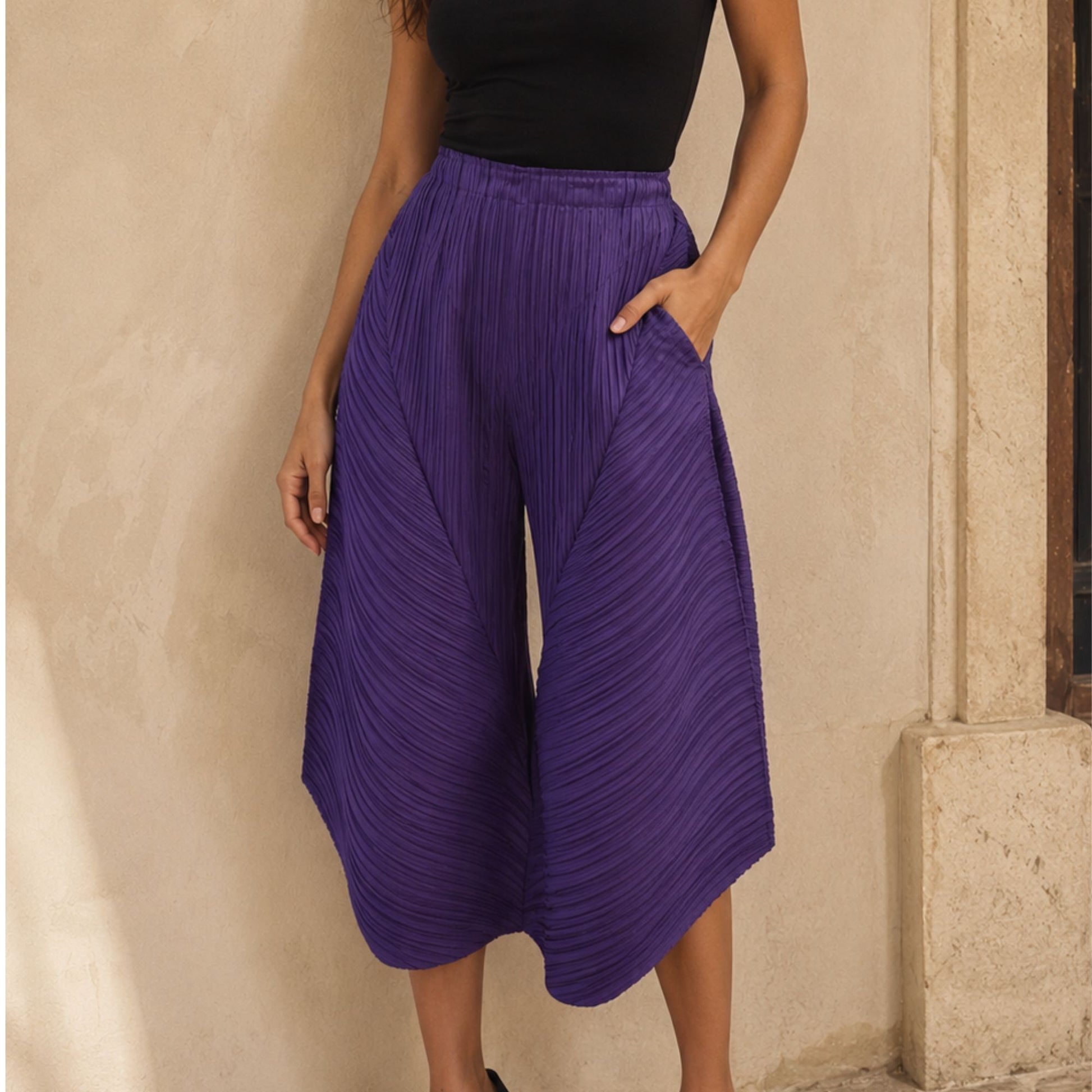 Person wearing purple pleated pants against a beige wall.