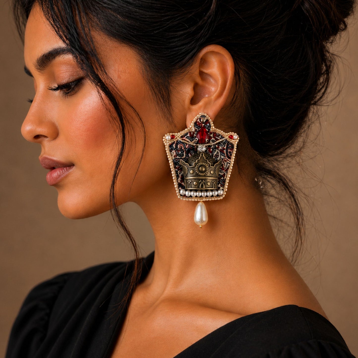 Close-up of a woman wearing an ornate earring that is shaped like a crown with red stones and faux pearls