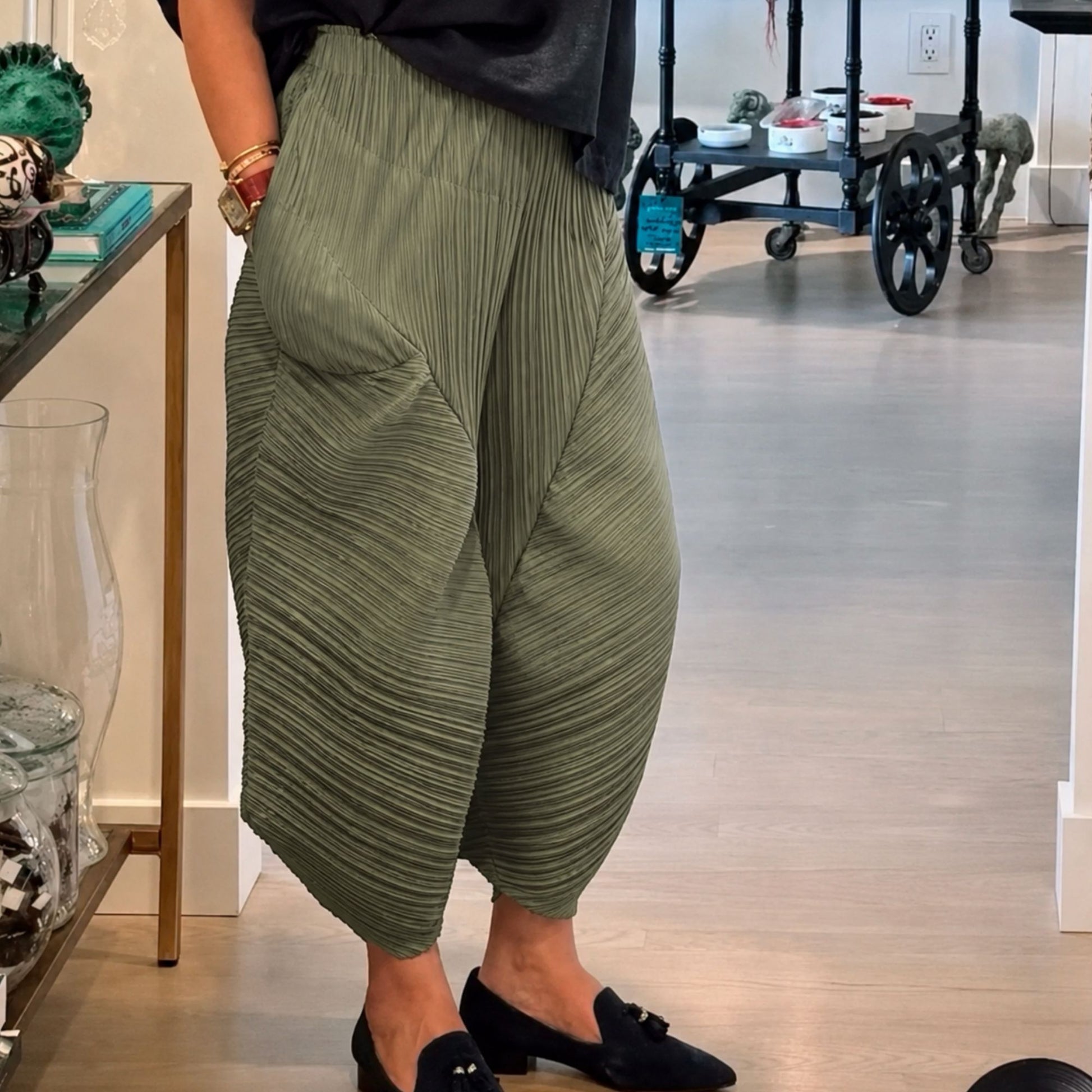 Person wearing green pleated pants in an indoor setting.
