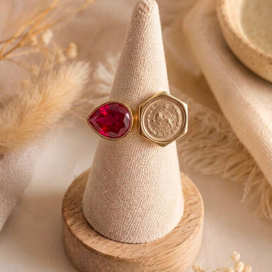 Vintage coin and ruby red teardrop crystal adjustable fashion ring displayed on a linen ring holder with a neutral boho background.