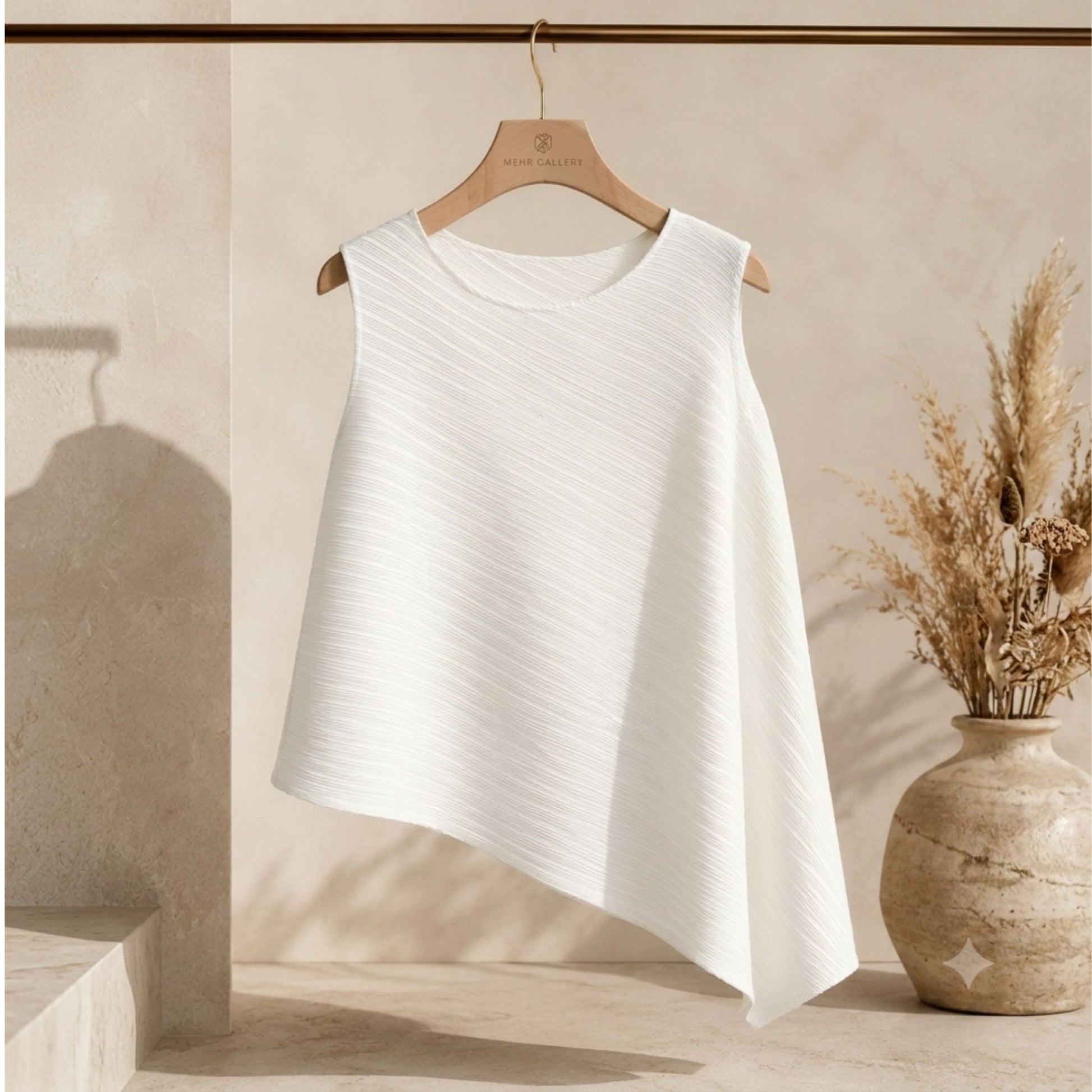 white pleated sleeveless top displayed on a hanger featuring an asymmetric hemline, crew neck, and wrinkle-resistant fabric.