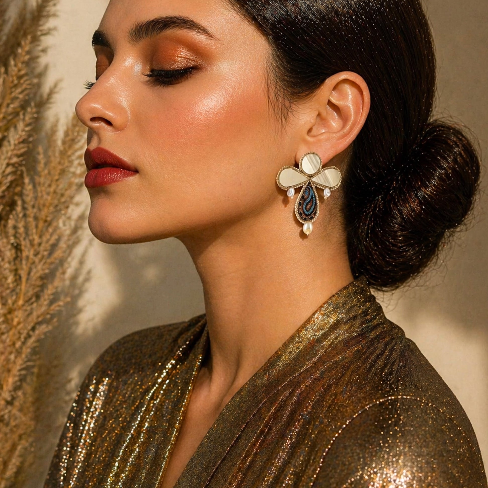 Close-up of gold tone Termeh paisley earrings with mirror detail and pearl accent