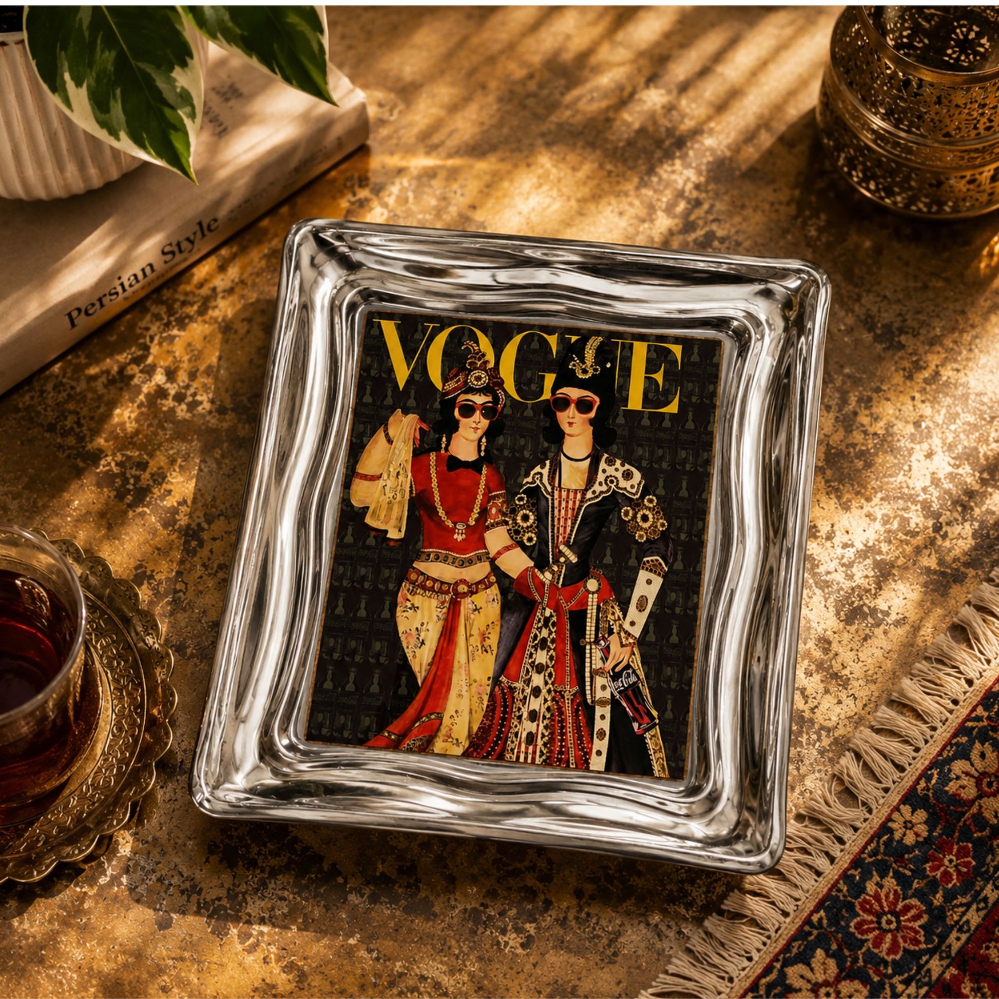 Vintage mini art and serving tray featuring a vintage Vogue-inspired design with nostalgic old Iran fashion artwork. Polished metal tray, 7 × 5 inches on a gold tabletop with a book, plant, tea cup, and decorative lantern around it.