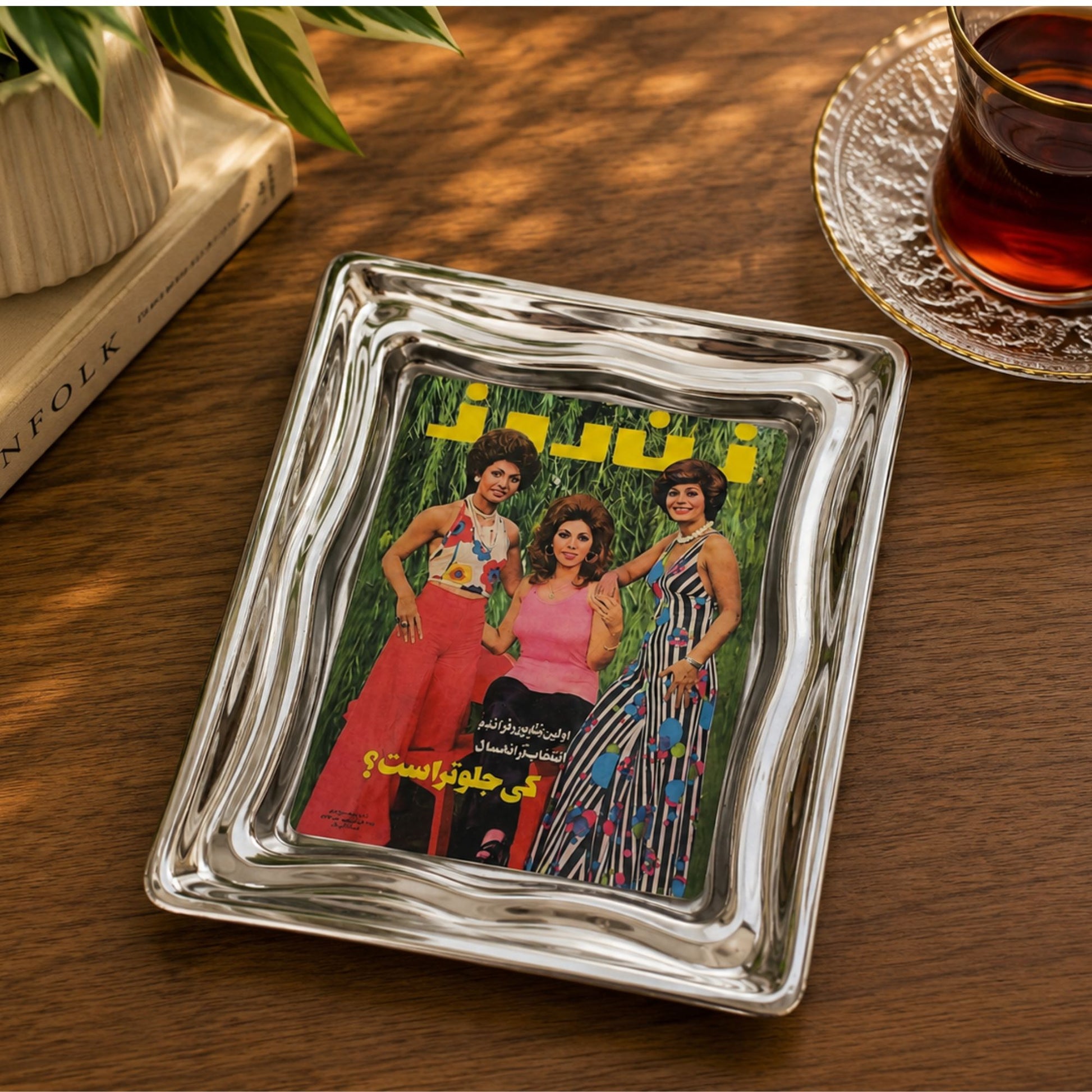 Vintage mini art and serving tray featuring the nostalgic Zan-e Rooz magazine cover design inspired by old Iran. Polished metal tray, 7 × 5 inches on a coffee table next to a glass of tea and stacked books.